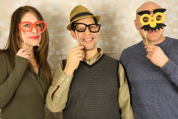 Two men and a woman at a photobooth, wearing funny props